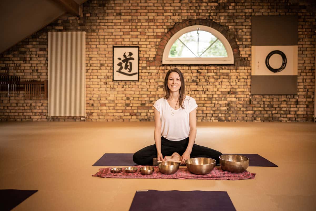 Eden Bratoljic sitzt vor Klangschalen die einer bunten Unterlage stehen