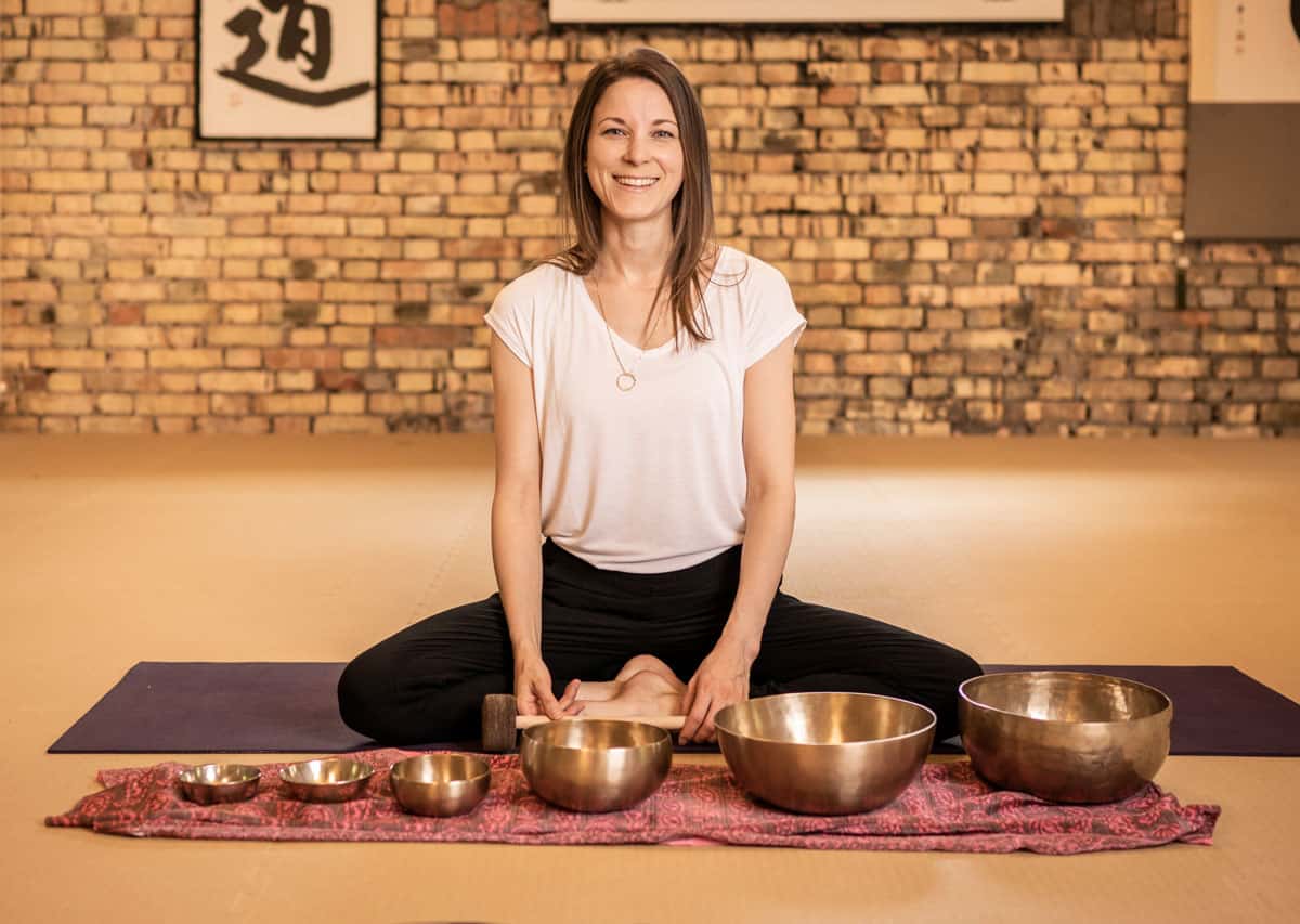 Eden Bratoljic sitzt vor Klangschalen die einer bunten Unterlage stehen